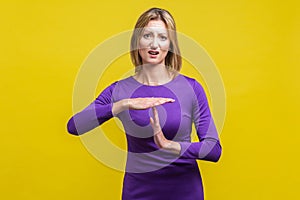 I need more time. Portrait of young woman showing time out or pause gesture. indoor studio shot  on yellow background