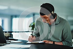 I need music to get me going. a young businessman doing paperwork while wearing headphones in an office at work.