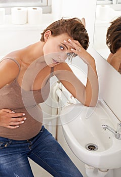 I need to quell this queasiness. a pregnant woman holding her stomach in discomfort in the bathroom. photo