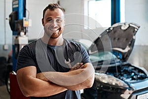 I opened up my own garage and its doing well. a mechanic posing with his arms crossed in an auto repair shop.