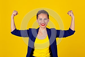 I am powerful and happy. Portrait of a happy elegant business woman showing power her biceps on yellow background. Multicultural