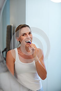 I prioritise my oral health, do you. an attractive young woman brushing her teeth in front of her bathroom mirror.