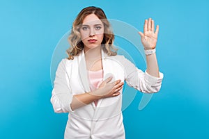 I promise. Portrait of beautiful woman making swearing gesture and holding arm on chest. blue background