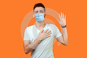 I promise. Portrait of serious brunette man with surgical medical mask standing with raised arm, swearing allegiance, taking oath