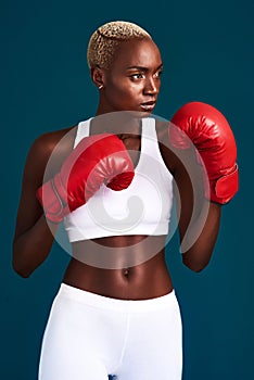 I am proud but never satisfied. an attractive young female boxer working out against a dark background in the studio.