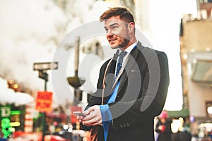 Am I at the right place. a young well dressed man texting on his cellphone while waiting for a taxi to get him to work