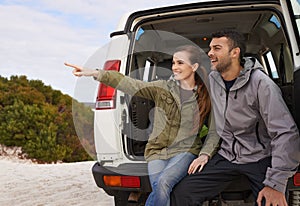 I say we go that way. a young couple at the back of their car while on a roadtrip.