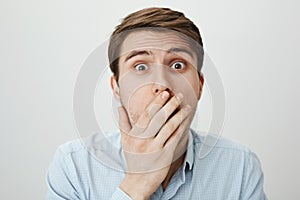 I am shocked to bottom of my heart. Portrait of terrified and amazed european male model covering mouth with palm while