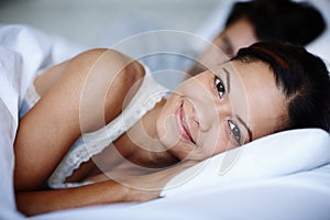 I slept so well...Smiling young woman lying in bed alongside her boyfriend.