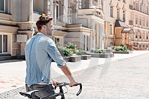 I am a slow walker, but I never walk back.Young brown-haired man standing outdoors with a bicycle and looking away.