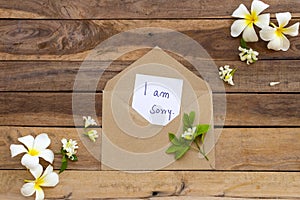 I am sorry message card handwriting in brown envelope with flowers frangipani