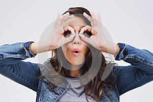 I spy with both my eyes. Studio shot of a young woman making a funny face against a gray background.