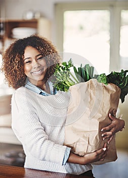 I stock my home with the healthiest food. Portrait of a happy young woman holding a bag full of healthy vegetables at