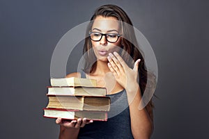 Am I suppose to study all of these. Studio shot of a young woman looking shocked while holding a pile of books against a