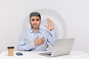 I swear! Honest businessman sitting office workplace with laptop on desk, raising hand, touching chest