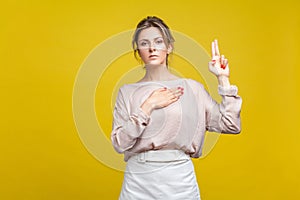 I swear! Portrait of faithful serious young woman with fair hair in casual beige blouse, isolated on yellow background