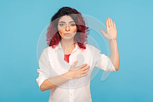 I swear! Portrait of hipster woman with fancy red hair holding hand on heart and raising palm to make oath