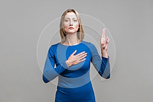 I swear! Portrait of honest citizen, young woman making loyalty promise. indoor studio shot isolated on gray background