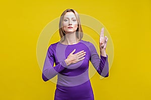 I swear! Portrait of honest citizen, young woman making loyalty promise. indoor studio shot isolated on yellow background