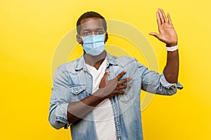 I swear! Portrait of honest serious man in denim casual shirt with surgical medical mask keeping hand on chest, raising palm,