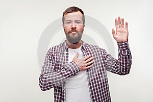 I swear! Portrait of responsible bearded man keeping hand on chest making promise. isolated on white background