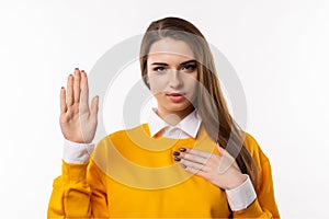 I swear. Portrait of sincere brunette girl raising one arm and hold hand on heart as give oath