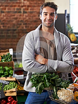I always take the healthy choice. Portrait of a young man in a grocery store holding a basket full of fresh produce.
