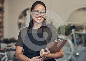 I take pride in my business. Shot of an attractive young woman standing alone in her bicycle shop and holding a