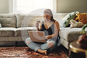 I think its time to top up on dog food. a young woman using a laptop and credit card in her living room at home.