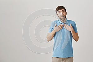 I am touched to my heart. Studio shot of pleased lovely bearded caucasian guy holding hands on chest while showing at