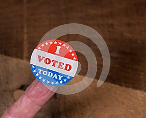 I Voted Today paper sticker on mans finger on rustic wooden table
