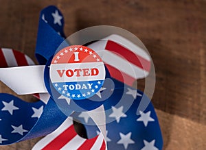 I Voted Today paper sticker on US Flag whirligig and rural wooden table