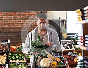 I only want the freshest. Shot of a young man walking in a grocery store with a basket full of fresh produce.