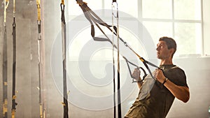 I want to have perfect body. Strong athletic man training his arms with trx fitness straps at gym.