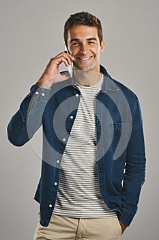 I was hoping youd call. Studio portrait of a young man talking on a cellphone against a grey background.
