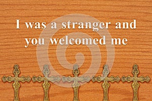 I was a stranger and you welcomed me message with bronze religious cross on wood