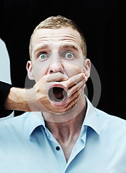 I will not be silenced. A distraught looking man with his mouth showing through the hand trying to silence him.