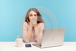 I will not tell anyone! Scared upset young woman employee sitting at workplace with laptop and covering mouth