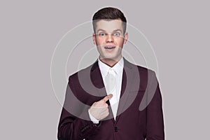 Am I winner?! Portrait of handsome amazed young man in violet suit, white shirt, standing, looking at camera, pointing himself wi