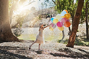 I wish these could fly me to the sky. a little girl playing with a bunch of balloons outside.