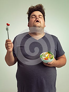 I wish this would turn into a burger. Studio shot of an overweight man holding a bowl of salad.