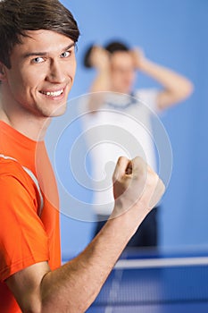I won! Happy young table tennis player gesturing while his opponent standing on the background with head in hands