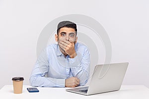 I won`t tell anything! Scared man employee sitting office workplace with laptop on desk, covering mouth