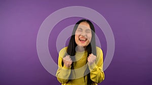 I won A tense Asian woman in a yellow sweater looks forward to the result and wins. woman on purple isolated background