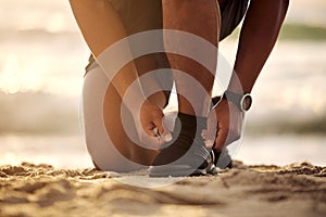 I wont allow myself to stumble. Closeup shot of an unrecognisable man tying his laces while exercising at the beach.