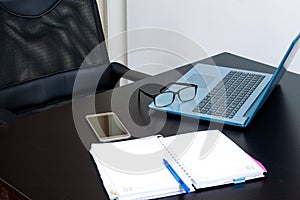 I work from home. Home table with a laptop, a notebook, glasses and cell phone. Side view