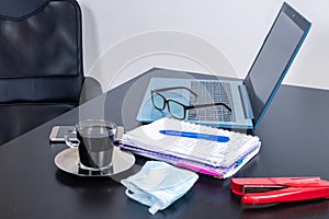 I work from home. Home table with a laptop, a notebook, glasses, coffee and cell phone. Side view