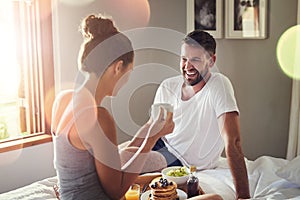 I wouldnt mind this everyday. a happy young couple enjoying breakfast in bed together at home.