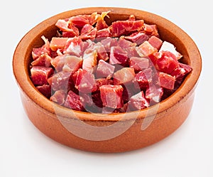 Iberian ham serrano cut into cubes diced. In clay bowl. Isolated on white background