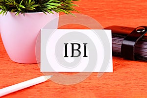 IBI symbol it is written on a white business card next to a business card holder, pencil and plants in a white pot photo